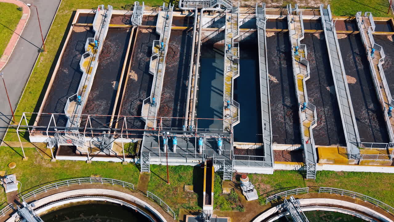 Top down view of rectangular primary sedimentation tanks at plant. Symmetrical aerial shot of parallel water treatment basins with metal walkways and mechanical equipment