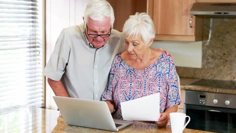 senior couple calculating their bills on laptop in the kitchen