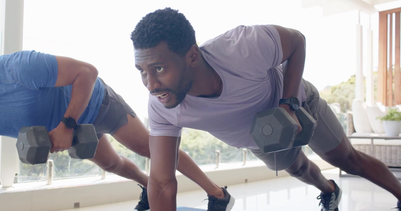 Asian and African American men starting plank, performing dumbbell rows near windows for core tone