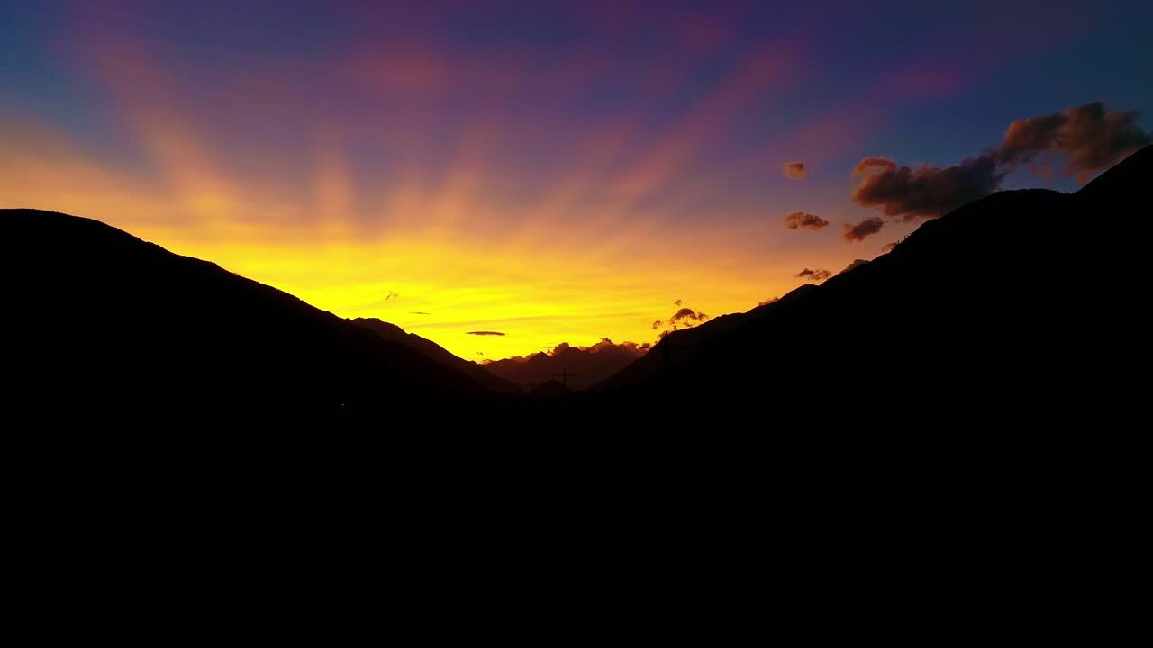 Sunset rays over dark mountain silhouettes - glowing golden sky at twilight hour
