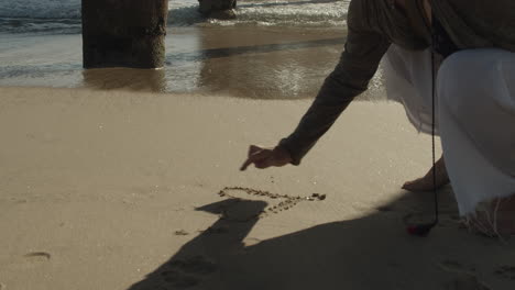 woman drawing a heart shape in the sand at the beach in cinematic slow motion