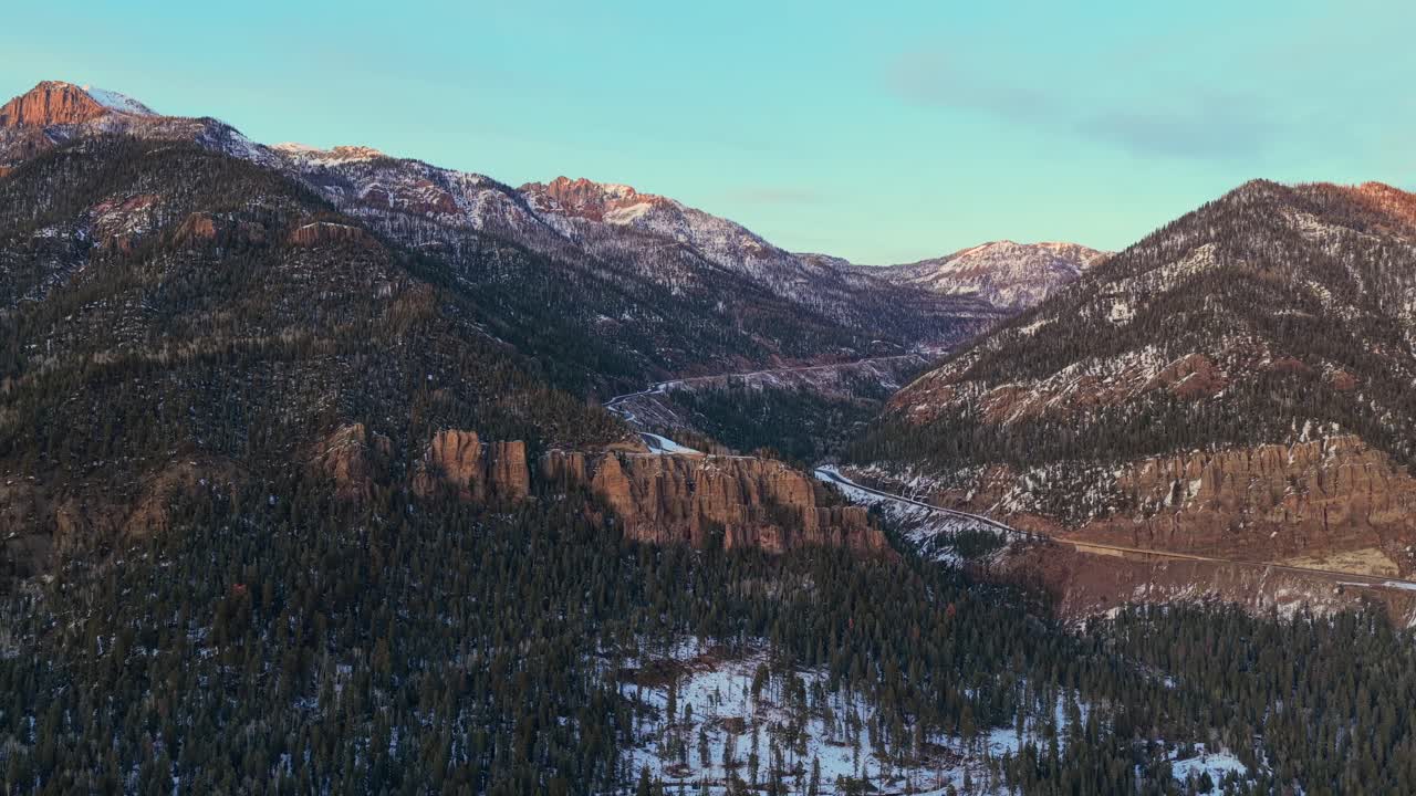 Ripresa aerea dall'alto angolo delle aspre Montagne Rocciose del Colorado al tramonto. La luce serale morente illumina le creste spolverate di neve e gli impervi canyon del valico montano ad alta quota.