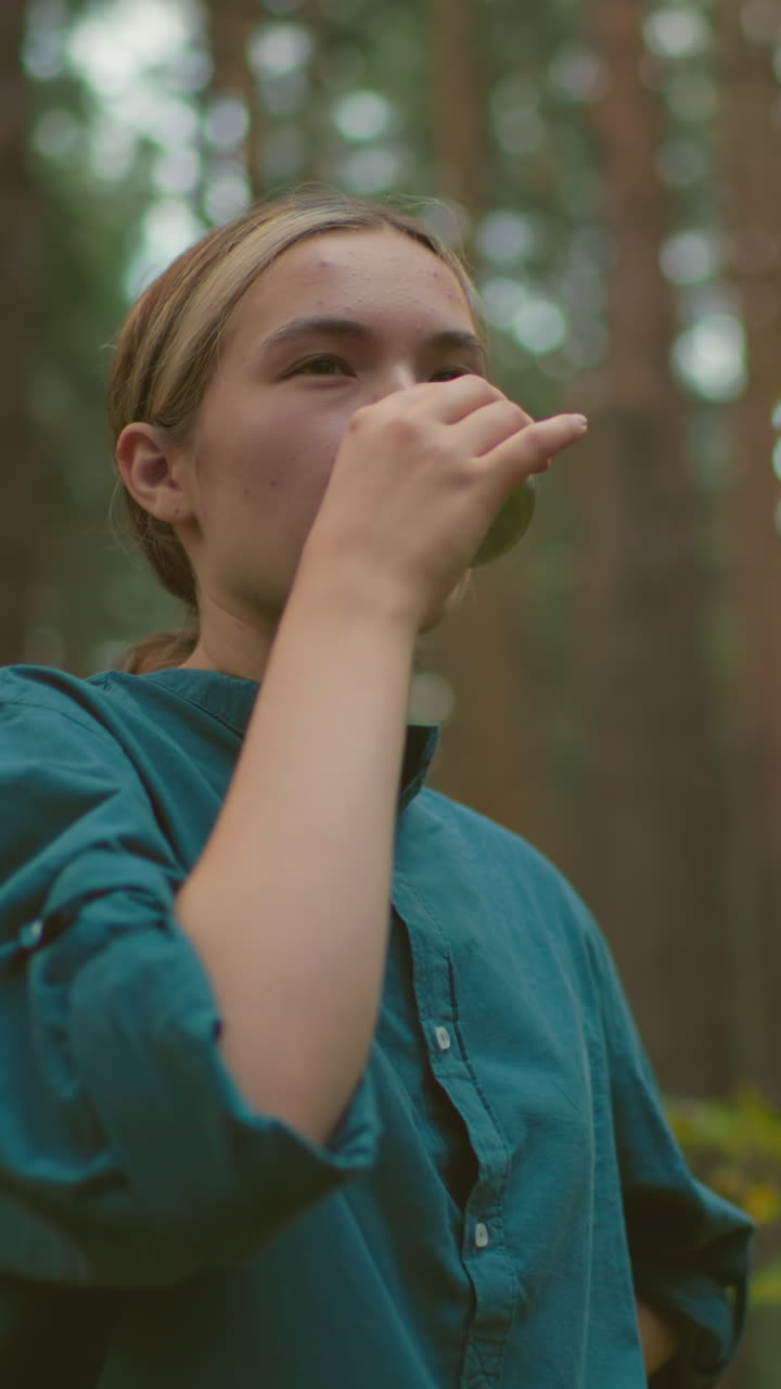 Two friends share peaceful moment in forest as one pours warm drink from thermos, her friend smiles and waits to receive it, surrounded by tall trees, they enjoy a serene outdoor break together
