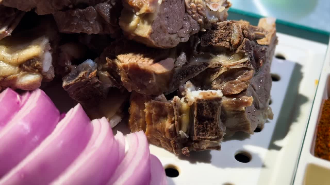 Close-up of a traditional Central Asia Altay Region lamb dish. Tender, cooked lamb pieces are served with sliced raw onion, a spicy chili oil dipping sauce, and a powdered cumin and chili spice blend