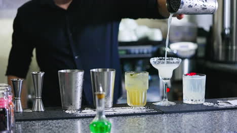 barman in black shirt filling the wineglass with beverage. glasses for cocktails making at the bar stand. close up. blurred backdrop.