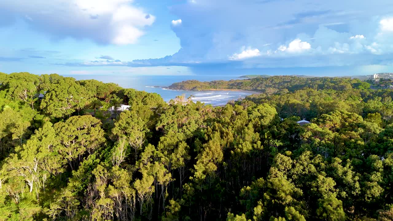 Drone footage captures lush forest and coastline at Charlesworth Bay Beach under bright daylight in Coffs Harbour, Australia
