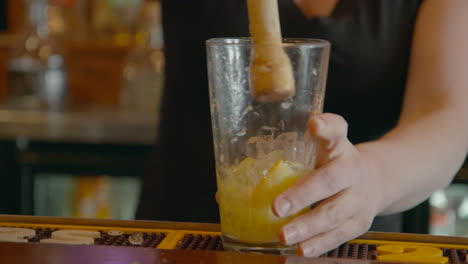 bartender making a cocktail crushing ice over lemon and limes in glass