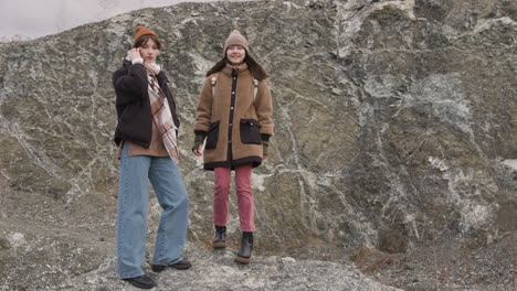 vista frontal de duas adolescentes em roupas de inverno posando para a câmera na montanha em um dia ventoso