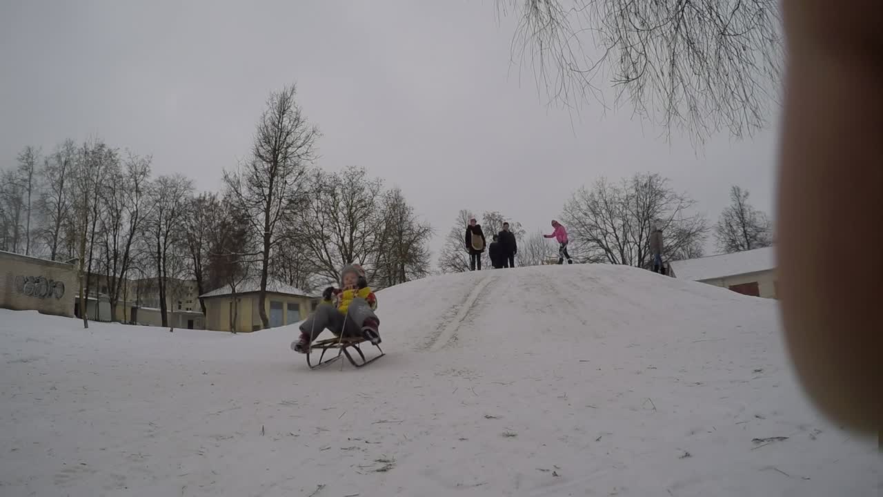 Bambina che scivola giù da una collina ghiacciata su una slitta durante le vacanze invernali.