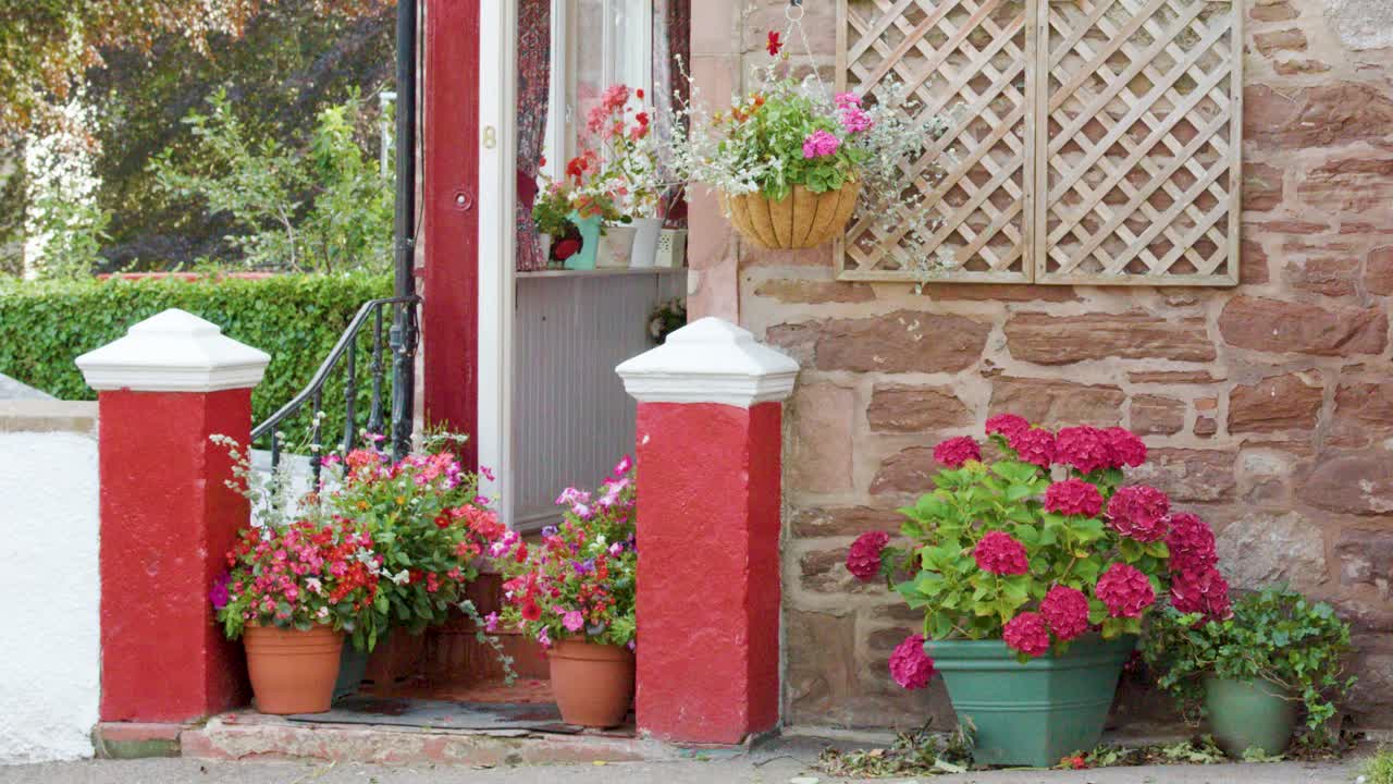 Camera pans over vibrant potted flowers beside a red stone house wall in Edinburgh daylight