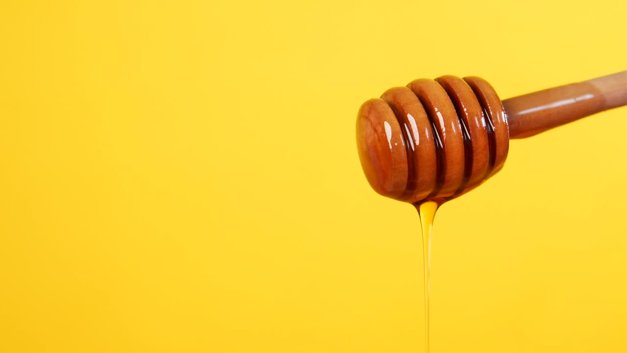 Miele che cola da uno spargimiele di legno su uno sfondo giallo
