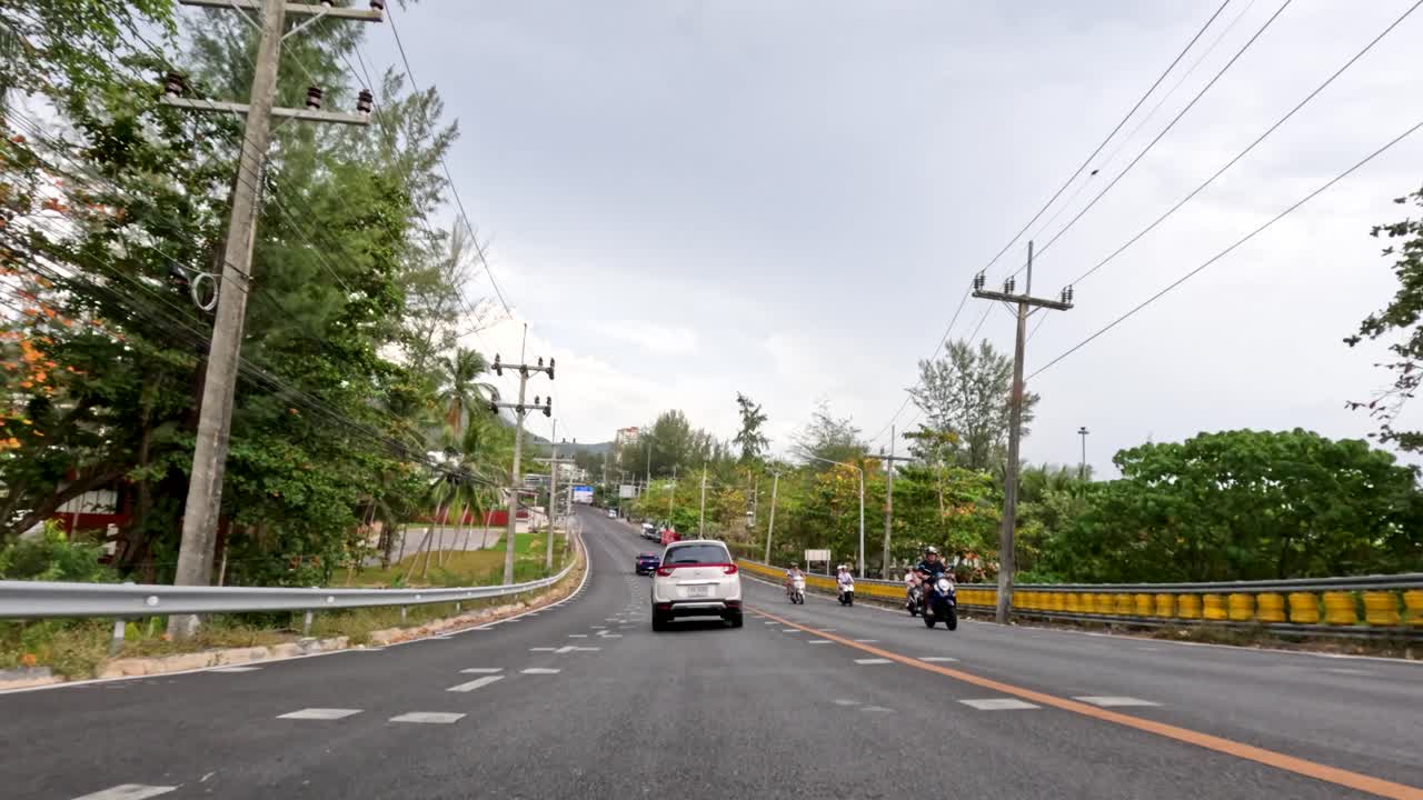 Car drives along tropical road with motorcycles, overcast daylight, wide dashcam perspective, smooth motion