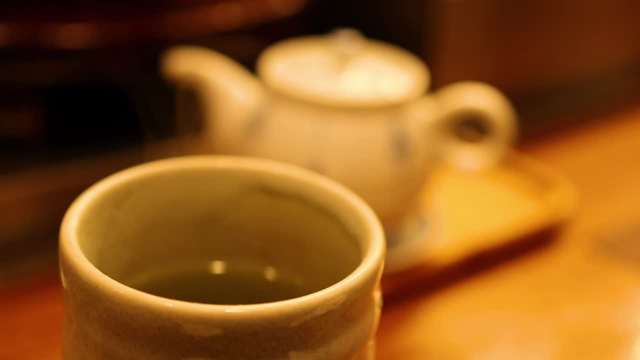A ceramic cup and teapot on a wooden surface, captured in warm lighting.