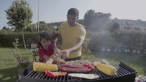 hombre feliz y su hijo preadolescente cocinando carne en la parrilla de barbacoa