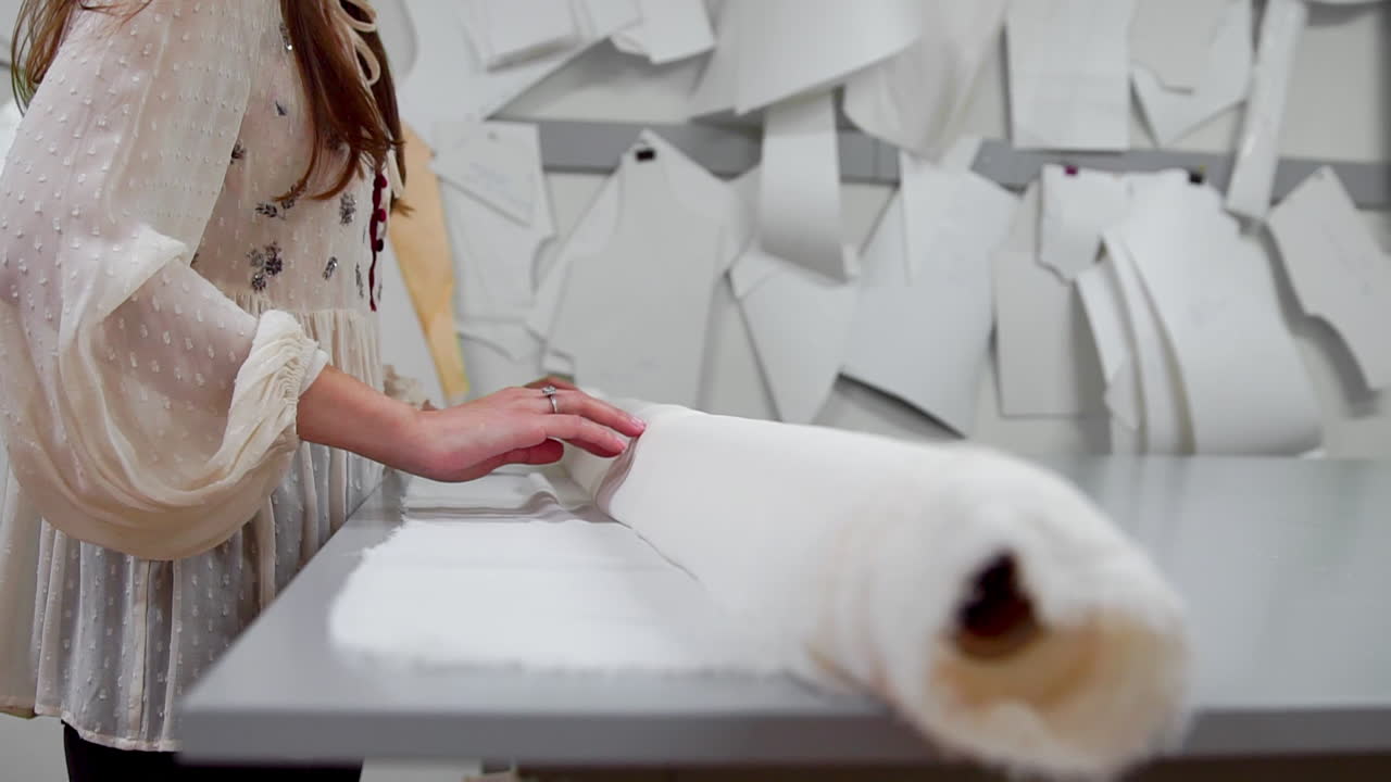 Clothing designer is working with measurements on a studio table. Shot on in 4K UHD . Closeup deploy a skein of white fabric in white and light-colored sewing in slow motion.