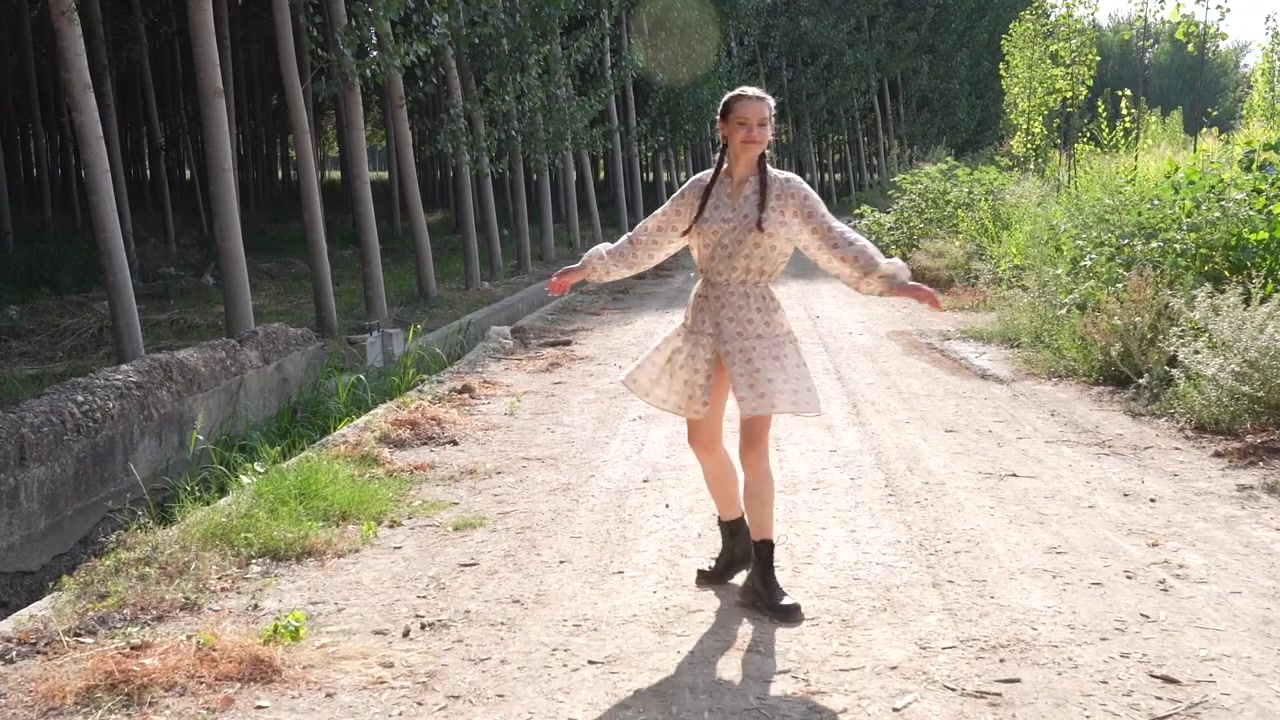 Un sentiero illuminato dal sole: una giovane donna cammina elegantemente con un bellissimo vestito floreale in mezzo alla natura.