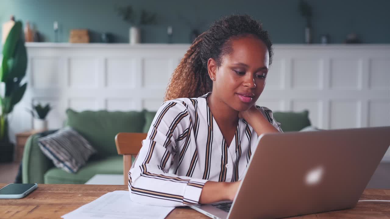 Young african american woman works with laptop and documents sits at table