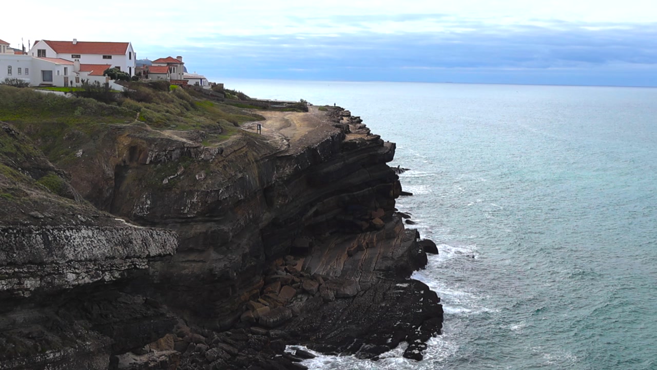 Dramatic Portuguese sea cliffs in Azenhas do Mar with waves crashing below and white houses with red roofs above.