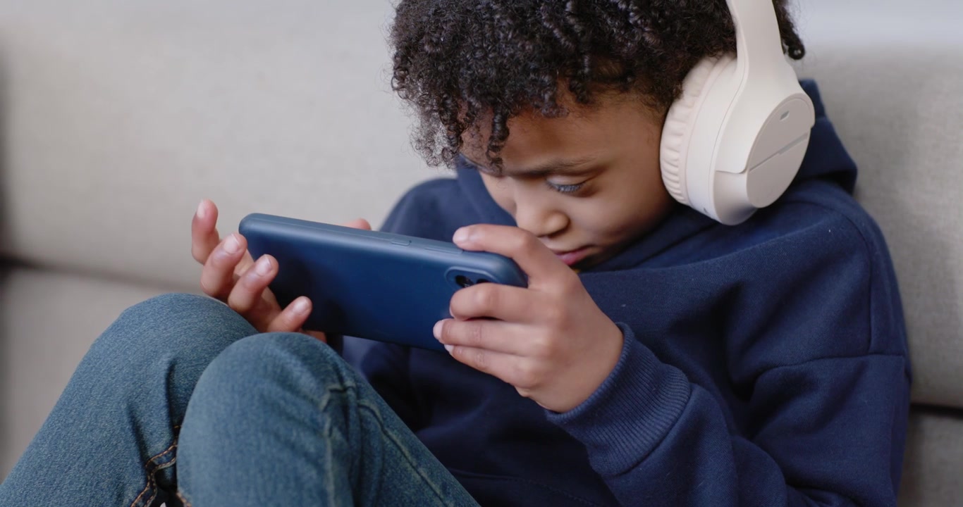 African American teenage girl holding blue tablet, wearing white headphones, adjusting grip on sofa