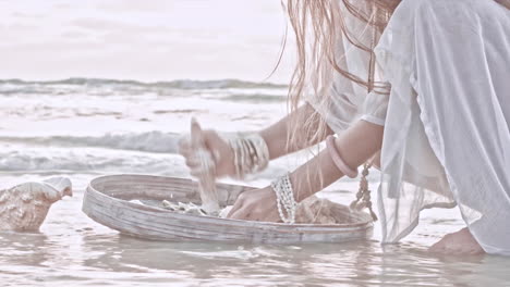 frau ohne gesicht, die in zeitlupe am strand eine paste mit muscheln herstellt