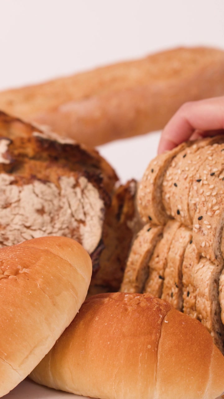 Close-up shot of hand selecting sliced multigrain bread from a variety of fresh loaves.