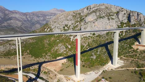 aerial shot of the fully finished moracica bridge in montenegro. the big red coat of arms of montenegro is seen on one of the bridge's pillar