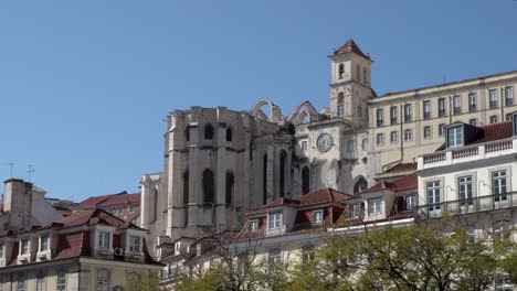 Carmo-Monastery-of-Lisbon,-view-on-the-apse-as-seen-from-the-Rossio-square,-drone-footage-from-a-distance-on-a-bright-sunny-day-with-blue-skies