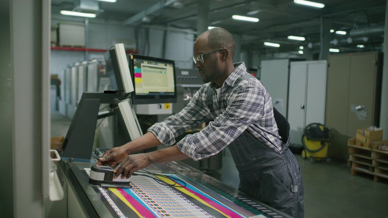Black Worker Using Spectrophotometer and Operating Machine in Printing House