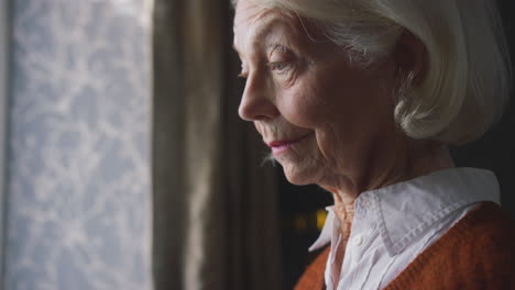 Senior-Woman-With-Hot-Drink-Trying-To-Keep-Warm-By-Radiator-At-Home-In-Cost-Of-Living-Energy-Crisis