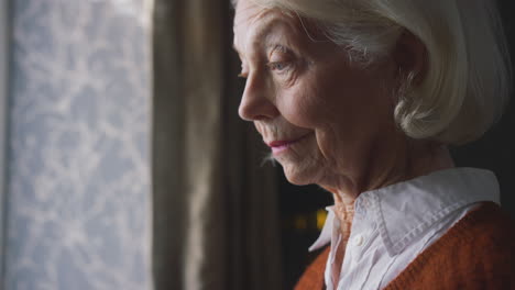 senior woman with hot drink trying to keep warm by radiator at home in cost of living energy crisis