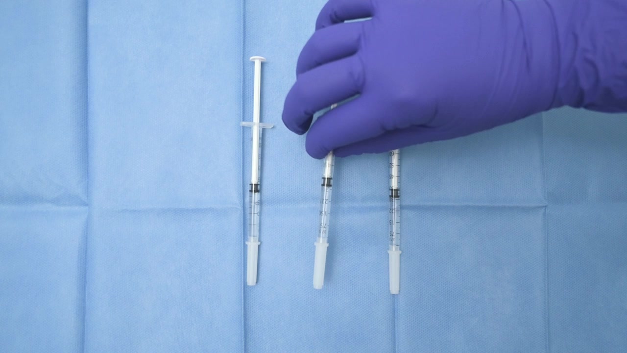 Medical professional in purple gloves taking a single use syringe from a blue sterile drape