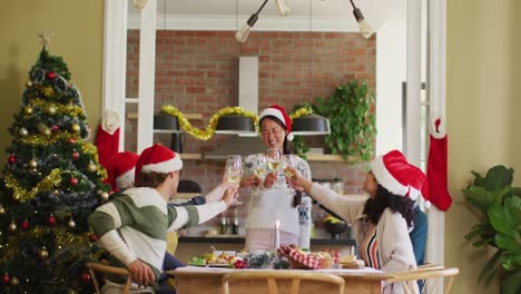 happy group of diverse friends in santa hats celebrating meal, toasting with vine at christmas time