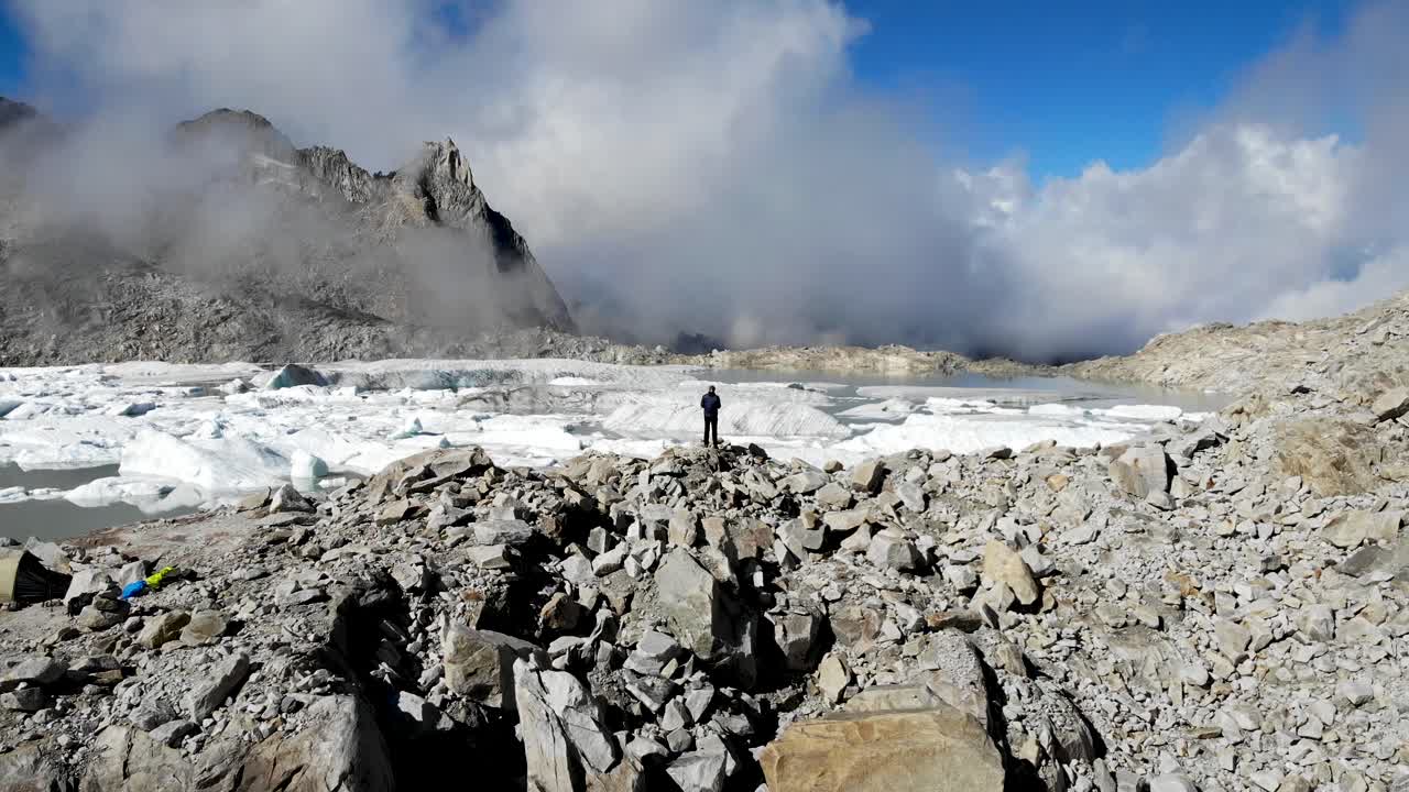 화창한 날 스위스 알프스의 외딴 지역에서 녹은 빙산으로 가득 찬 빙하 호수를 바라보는 등산객 위의 공중 비행