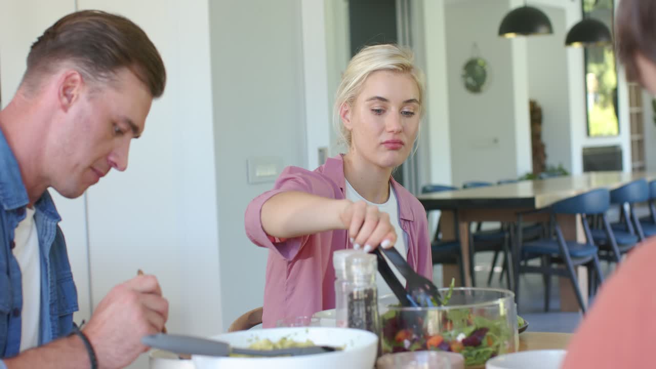 Family woman in pink top reaching meal starting adjusting grinder serving salad with tongs at table