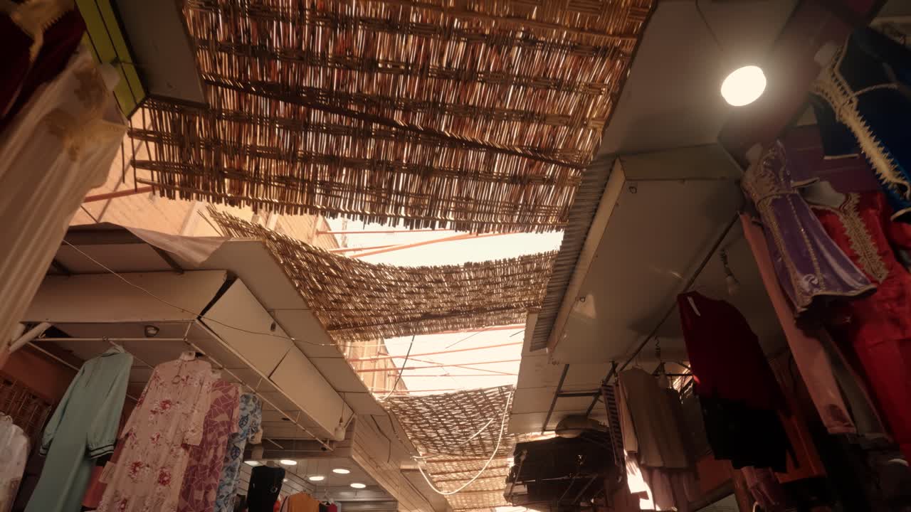 Woven reed roof panels filter daylight above clothing stalls in a traditional Moroccan market