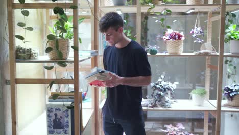 Young-male-student-walks-in-and-takes-borrows-books-from-the-library-bookshelve-looking-and-camera