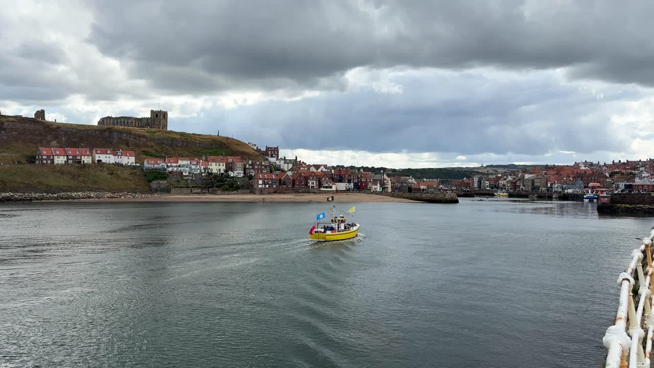Peschereccio giallo che rientra al porto con chiesa sulla collina in lontananza. Whitby - North Yorkshire, Regno Unito
