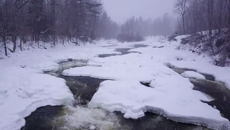 slow motion shot of icy river with small waterfall during snow storm