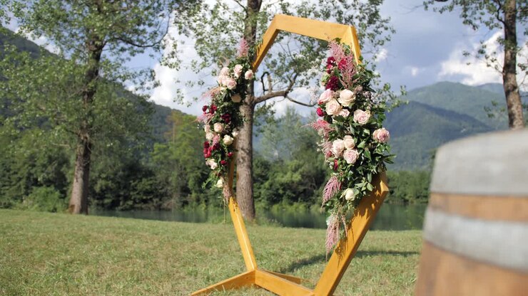sekskantet bryllupsbue med blomsterdekoration på mark ved sø før ceremoni