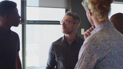 Four-male-creatives-stand-having-a-discussion-in-their-workplace,-close-up,-selective-focus