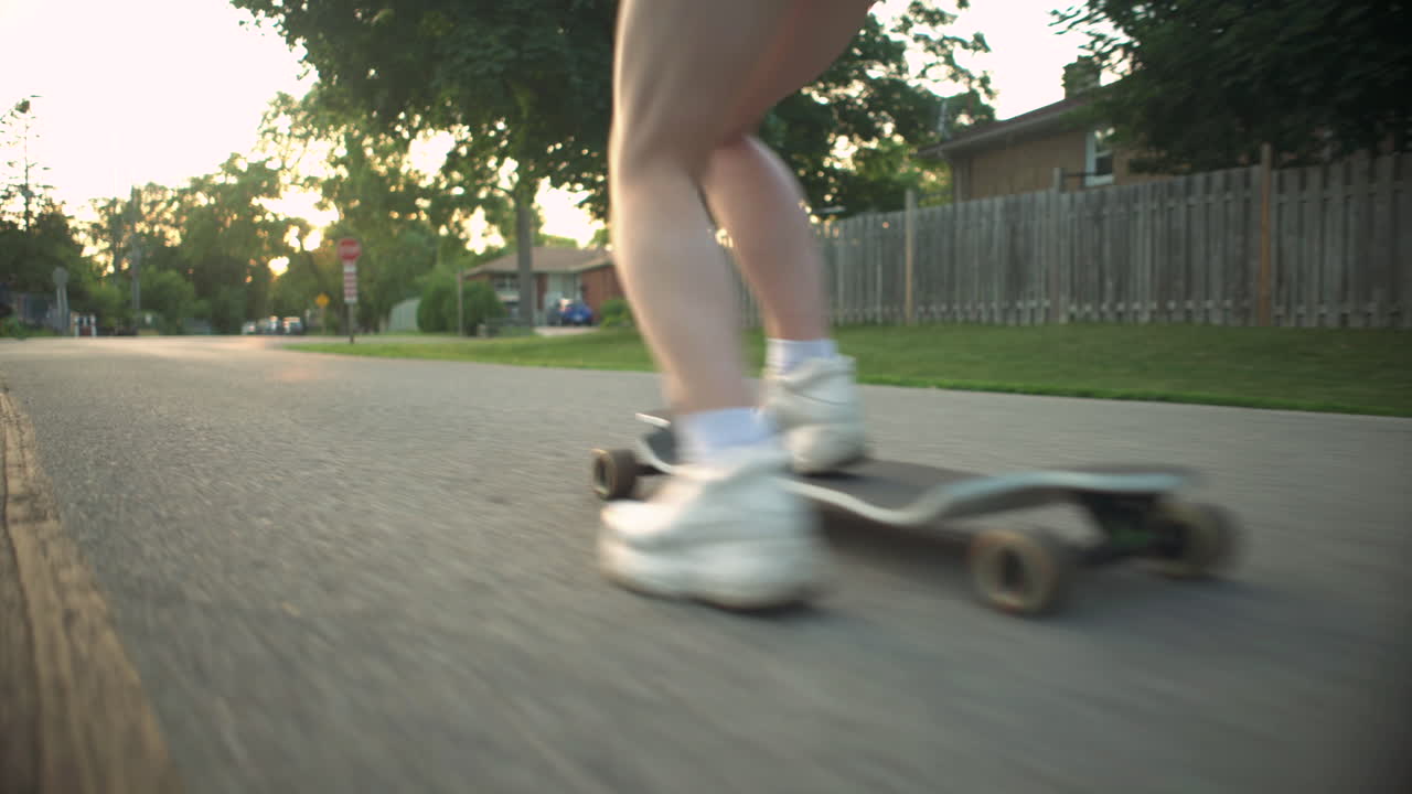 Girl's legs as she rides longboard at golden hour down residential neighborhood