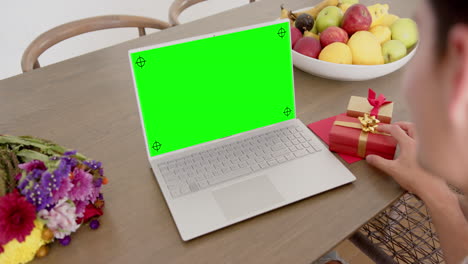 caucasian woman holding red gift using laptop with copy space on green screen