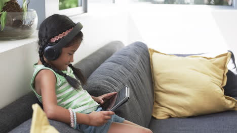 biracial girl with headphones uses a tablet on a couch