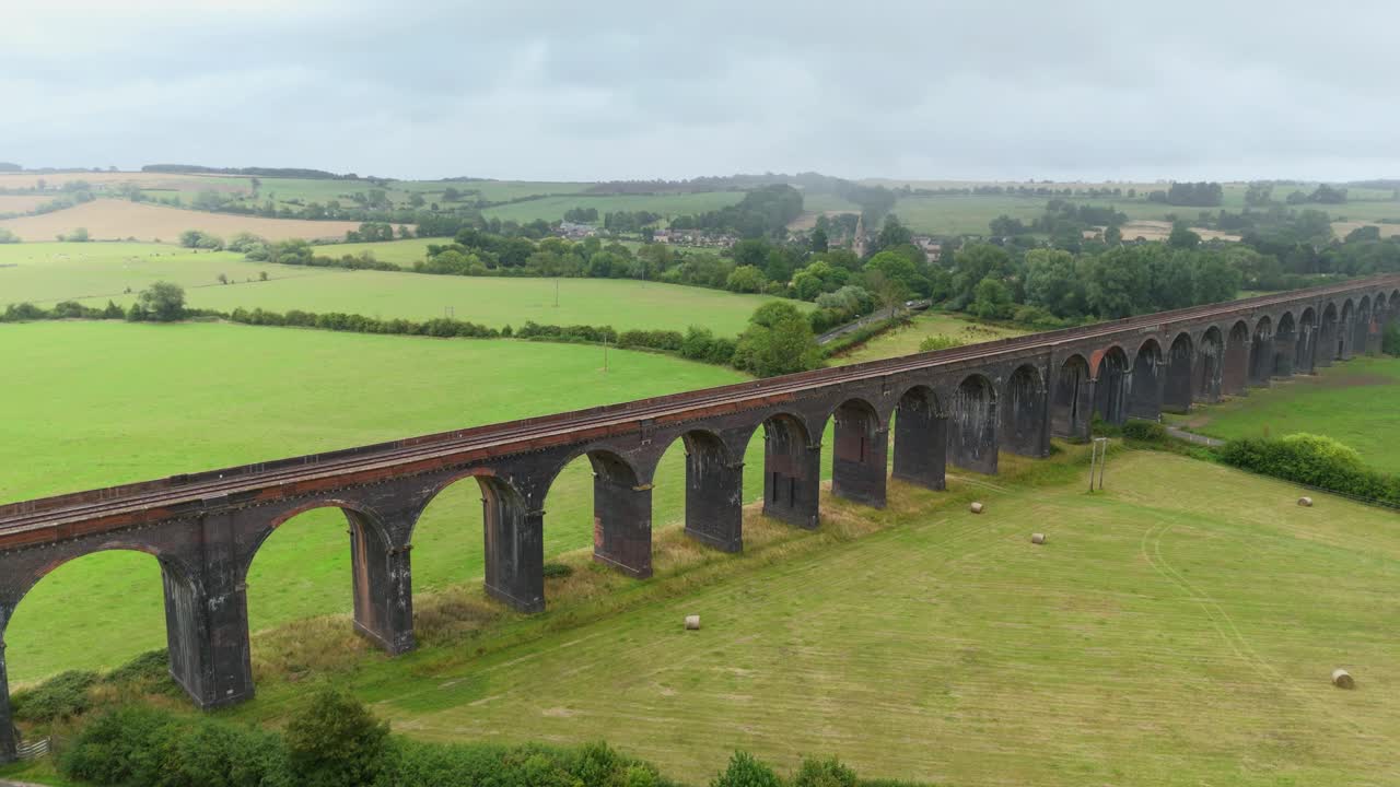 Drone aerial cinematic orbit view of historic Harringworth Viaduct railway bridge with arches and rural wetland landscape Corby England United Kingdom