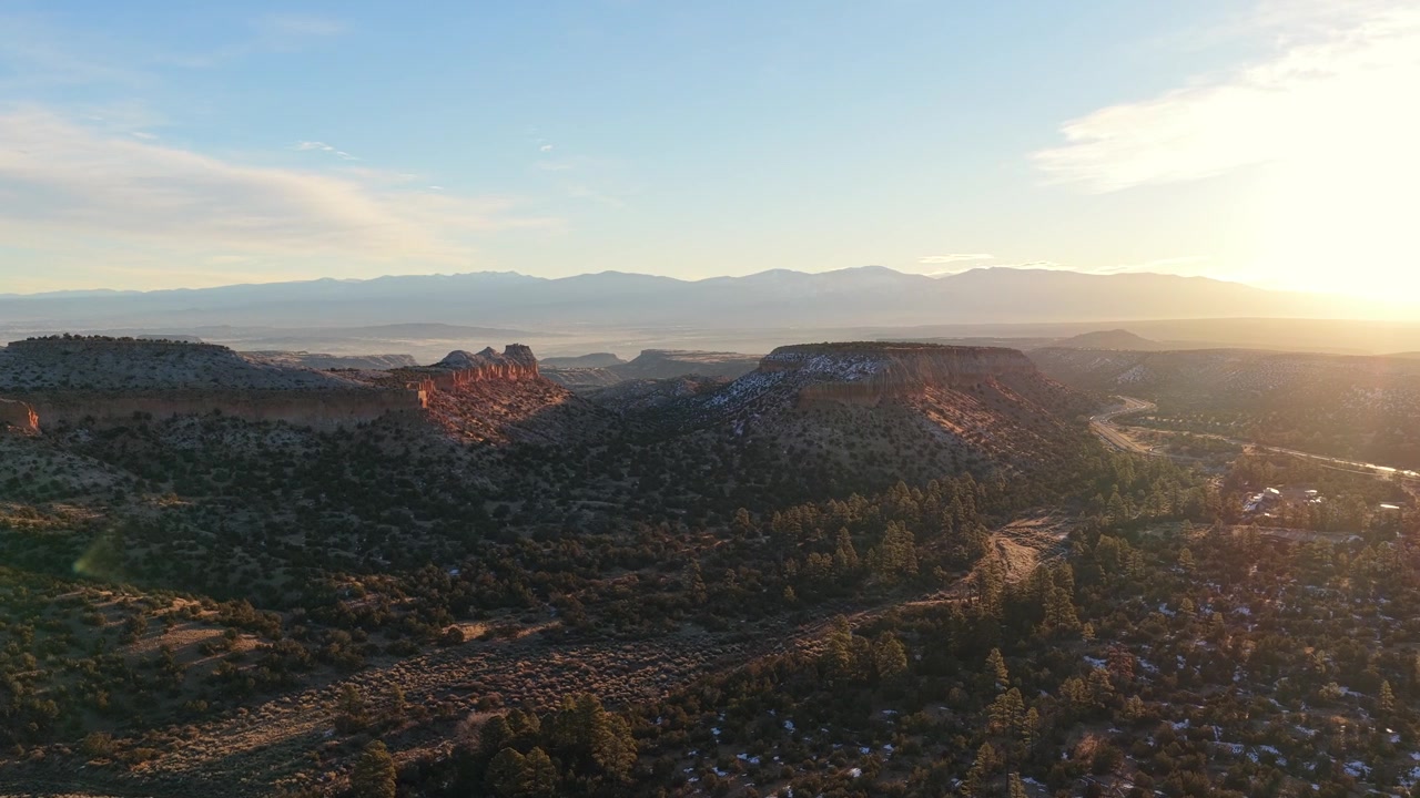 Vista aerea 4K che mostra mesas aspre vicino all'ingresso della città di Los Alamos. La luce del sole dell'ora d'oro illumina le ripide pareti rocciose, evidenziando la neve sparsa attraverso il terreno desertico d'alta quota