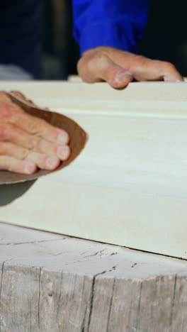 master is polishing a wooden product with an emery cloth by his hands on a stump in the street in the afternoon. vertical video