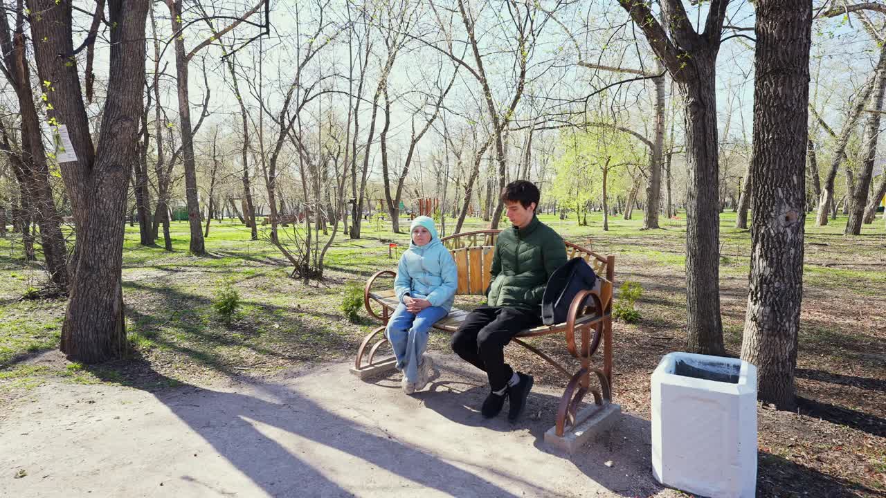 Young Man and Girl Sitting on a Bench in a Sunny Spring Park