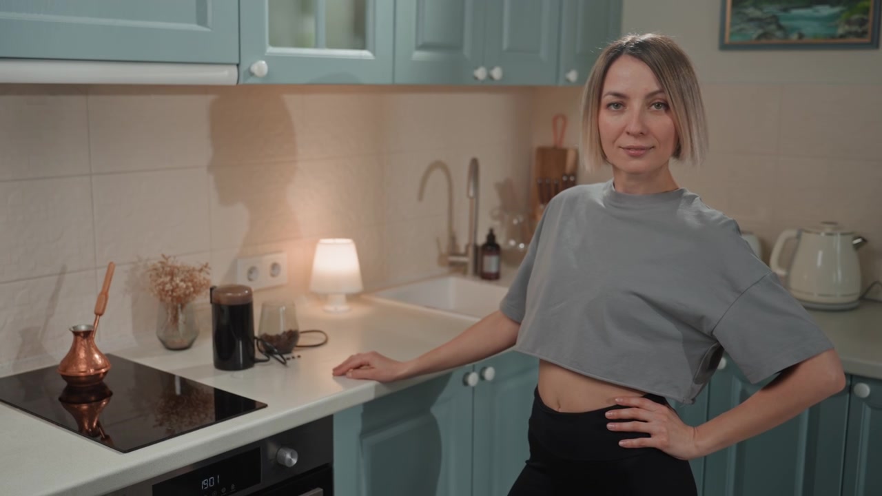 Caucasian woman in pastel kitchen, striking playful confident poses with hand on hip and bob haircut catching warm lamp light, upbeat musiclover energy and content creator style, cozy domestic scene