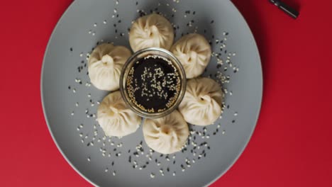 Composition-of-plate-with-dim-sum-dumplings-and-chopsticks-with-soy-sauce-on-red-background