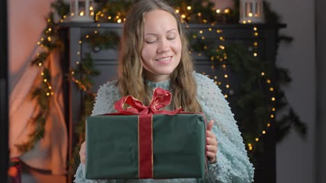 woman listens with curiosity as she shakes a christmas present, surrounded by festive decorations at home